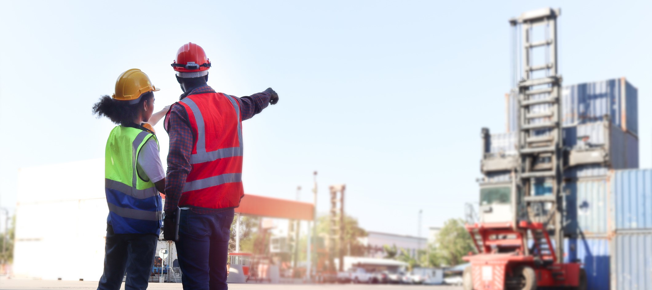 A male and female construction worker point towards a stack of shipping containers